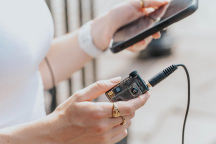 Piccolo dispositivo audio in plastica trasparente fumé con rotella e presa jack da 3,5 mm, collegato a uno smartphone, vista ravvicinata
