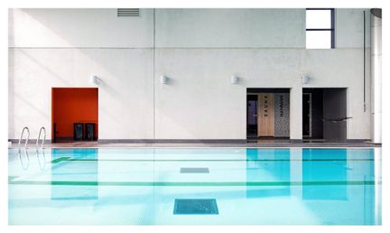 Rektangulær indendørs pool med turkisfarvet vand, metaltrappe, farvede døre, grå beton, spotlights