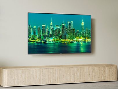Panasonic TX-65LX700E-fladskærms-tv, der viser et billede af oplyste skyskrabere om natten, stående på et lyst trækabinet