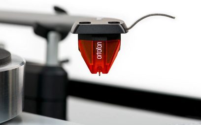 Lysande röd pickupcell monterad på en metallisk tonarm på en lackad valnötsfanerad skivspelare Thorens TD 1500
