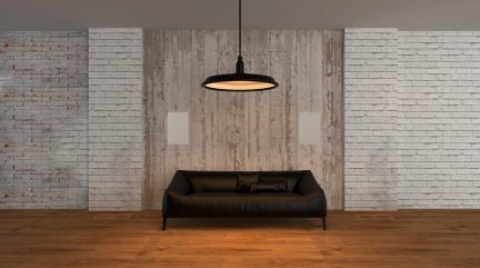 Schwarzes 2-Sitzer-Sofa aus Leder oder Kunstleder auf Parkettboden, vor weißer Ziegelwand, unter schwarzer runder Hängeleuchte