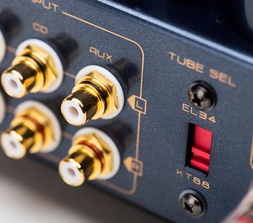 Skråt nærbillede af et antracitgråt metalpanel med fire guldbelagte RCA-stik med hvid kant og en rød vælger til EL34/KT88-rør