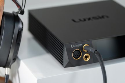 Luxsin fekete hi-fi fejhallgató-erősítő alumínium előlappal és aranyozott jack aljzatokkal, bal oldalon audiófil fejhallgató
