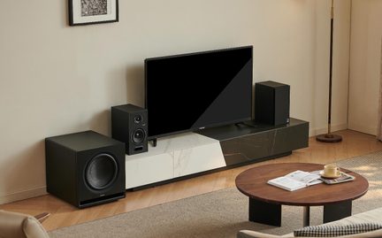 Černý televizor na nízkém nábytku s černobílými mramorovými panely, dvě reproduktory a subwoofer, šikmý pohled