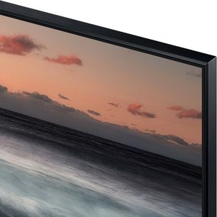 Samsung QE65Q900R-tv, der viser en orange, skyet himmel ved solnedgang, der spejler sig i et roligt hav