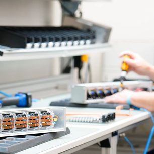 Wielogniazdowa listwa przeciwprzepięciowa Inakustik AC-3200 Filter Digital SCHUKO w aluminiowej, srebrnej obudowie, widok z trzech czwartych na stole warsztatowym, z odkręconą pokrywą odsłaniającą cztery wewnętrzne moduły ułożone w rzędzie oraz ich wielokolorowe okablowanie