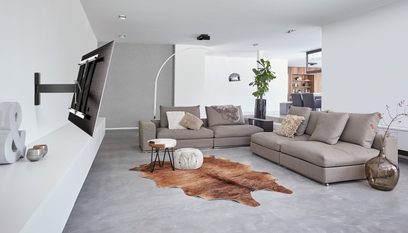 Moderne stue med grå hjørnesofa, kohudsløber, grønne planter, træhylder og vægmonteret fladskærm