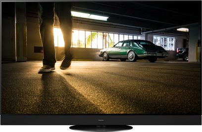 Gammel grøn bil parkeret i et mørkt garage, set fra siden, med tændte forlygter der oplyser det ru betonlgulv