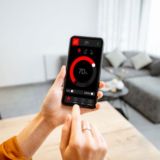 Hovedperson holder en smartphone, der viser en sort brugerflade med en rød cirkel, der angiver 70 %, en finger peger mod skærmen, sløret baggrund.