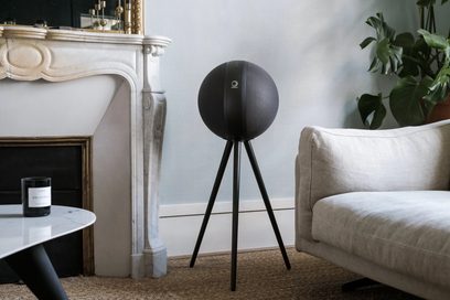 Trådløs, tilsluttet Elipson Planet W35+ sort højttaler på stativ, set forfra i et indendørsmiljø, med sofa og plante i baggrunden
