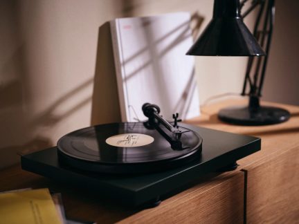 Črna vinilna platina z pravokotno podstavo, črnim ramenskim mehanizmom in črnim diskom, pogled iz treh četrtin na pohištvo iz lesa