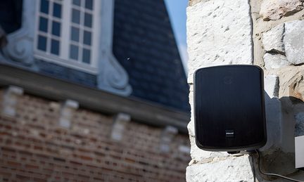Cassa acustica da esterno nera Apart Audio montata a parete su facciata in pietra di un edificio storico