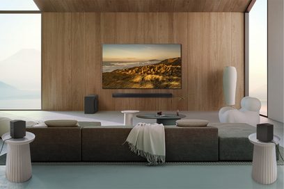 Samsung F-HW-Q995D-BF soundbar under vægmonteret skærm, grå sofa, hvide runde borde, hvid lænestol, trævæg