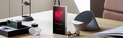 Czarny cyfrowy odtwarzacz audio z frontem ze szkła i srebrną metalową obudową, widok z przodu pod kątem, włączony ekran dotykowy, trzy przyciski sterujące po prawej stronie oraz podłączony kabel słuchawkowy na górnej krawędzi