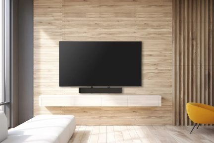 Svart veggmontert TV med lydplanke og hvit vegghengt TV-benk, i en stue med sennepsgul lenestol