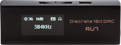 Bærbar Cayin RU7 lydkonverter i sort aluminium, set forfra, kompakt rektangulært kabinet med OLED-skærm til venstre, gyldne påskrifter «Discrete 1 Bit DAC» og RU7 til højre, volumenknapper +/− og modeknap på øverste kant