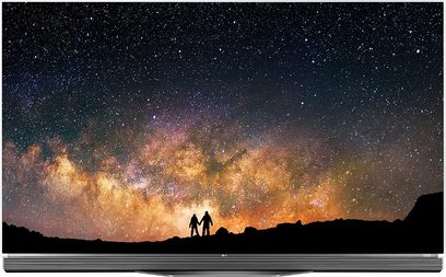 Nattehimmel med stjerner og den orangefarvede mælkevej over silhuetter af bjerge, to personer står i forgrunden