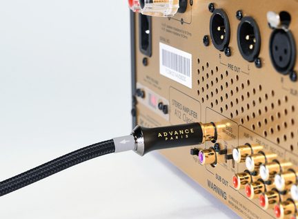 Blank høyglanset RCA-kontakt «Advance Paris» med sort flettet strømpe tilkoblet, nærbilde i trekvart vinkel av bakpanelet på en stereoforsterker i gullanodisert metall med rekker av RCA-innganger og forgylte XLR-kontakter