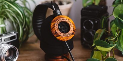 Åben hi-fi hovedtelefon Grado GS3000e i træ, sort gitter, placeret på et træbord med grønne planter og et analogt kamera
