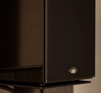 Kompakt sort højtaler med lakeret kabinet og stofgitter, PSB-logo nederst, set i trekvartsprofil, på metalstativ