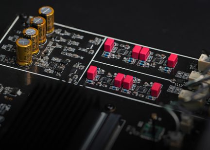 Črna elektronska plošča z zlatimi cilindričnimi kondenzatorji, rdečimi pravokotnimi komponentami in vidnimi tiskanimi vezji.