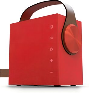 Kannettava Morel Biggie -bluetooth-kaiutin rubiininpunaisena metallisena versiona, kolmen neljäsosan kulmasta kuvattuna kevyessä alaviistossa, sileä kuutio ruskealla kaarevalla nahkakahvalla, suuri harjatusta alumiinista valmistettu pyöreä säätönuppi oikeassa kyljessä ja pystysuoraan etupaneeliin asetellut kosketuskuvakkeet