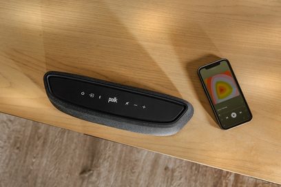 Polk Audio MagniFi Mini AX-soundbar og dens fjernbetjening, set forfra på en lys træoverflade