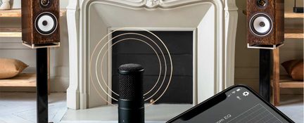 Houten luidsprekers op zwarte standaards, zwarte centrale microfoon, wit gebeeldhouwd haard, smartphone met zichtbaar scherm