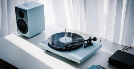 White vinyl turntable with black record, tonearm and matching compact speaker on white table