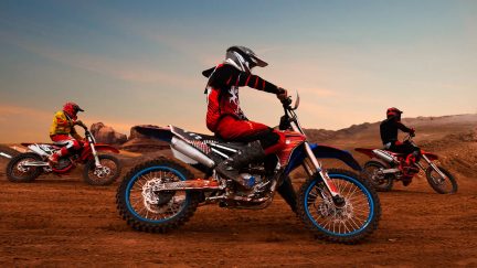 Motocross i ørkenen ved solnedgang, tre kørere i aktion springer på motorcykler, set fra siden