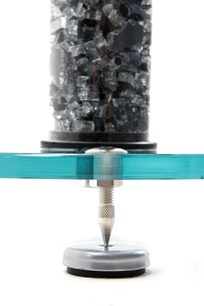 Højttaler-fod fra Atacama Audio Aurora 6 i børstet aluminium, med cirkulær base og cylindrisk søjle, toppet med en glasbeholder fyldt med grå granulater