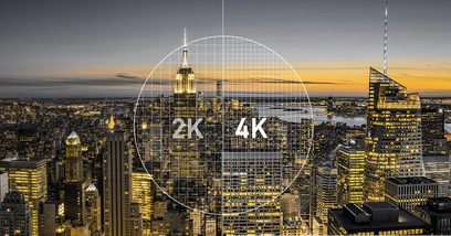 Natfotografi af en oplyst by med skyskrabere, med en cirkel ovenpå indeholdende "2K 4K" i hvidt