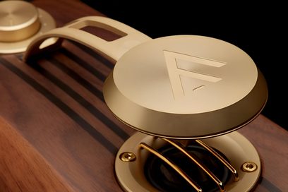 Primo piano obliquo del super-tweeter Fyne Audio SuperTrax in metallo dorato, cappuccio rotondo con logo, braccio traforato, su cassa in legno