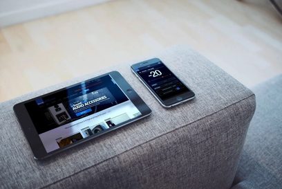 SVS SB-2000 Pro vit lackerad subwoofer och smartphone som visar kontrollappliktionen, placerade på en grå tygduk