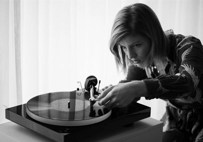 Ung kvinde med blondt hår, hænder på sort vinylplade, koncentreret ansigtsudtryk, kontrastfyldt sort-hvid belysning