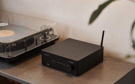 Preamplificator audio din metal, negru mat, cu buton, mufă jack și antenă, vedere din trei sferturi, pick-up în stânga