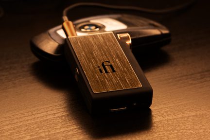 Sort, rektangulært kabinet med børstet metalplade, "iFi"-logo, forgyldt stik, placeret på en sort, afrundet genstand