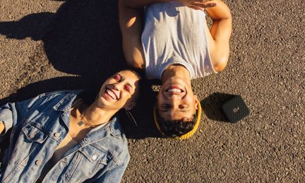Due persone distese sulla schiena, sorridenti, una indossa una maglietta grigia, l'altra una camicetta blu con motivi bianchi