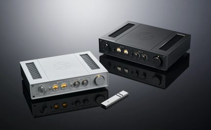 Два чорних аудіопідсилювачі hi-fi, один над одним, з золотистими кнопками та роз'ємами, та білий пульт дистанційного керування