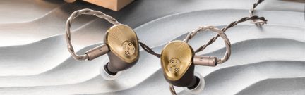 To guldfarvet, snoede in-ear hovedtelefoner med silikoneørepropper, liggende på en lys gråbølget overflade
