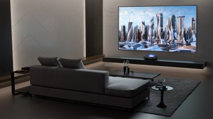 Moderne stue med grå sofa, sort sofabord, projektor, vægskærm, sidebord, vase, figur, glas
