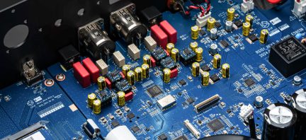Elektronisk kort set ovenfra med gule cylindriske kondensatorer, metalstik, integrerede kredsløb og røde komponenter