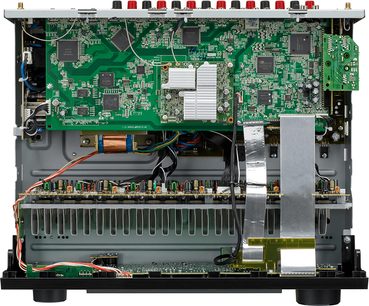 Indvendigt syn af en sort Denon AVR-X3500H-forstærker, grønt printkredsløb med elektroniske komponenter, kølelegemer og ledningsføring