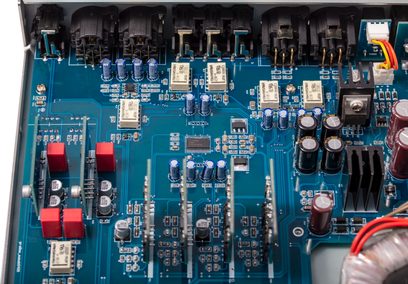 Modrý tištěný spoj s různými elektronickými součástkami, včetně červených a černých kondenzátorů, v kovovém pouzdře