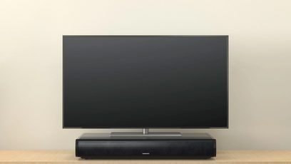 Onkyo LS-T10 schwarze Soundbar vor einem Fernsehbildschirm, Frontalansicht auf einfarbigem beigem Hintergrund
