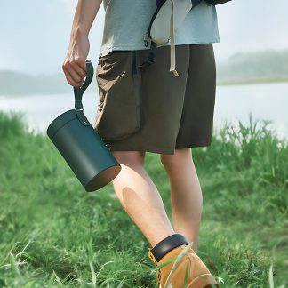 Person i brune shorts og grå t-shirt, der holder en grøn cylinder med håndtag, går på græs, gule sko