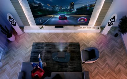 Proiettore home cinema nero su tavolino basso, vista dall’alto, videogioco di corse su grande schermo