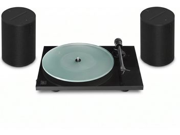 Svart vinylspelare med transparent tallrik och tonarm till höger, flankerad av två svarta Sonos-högtalare