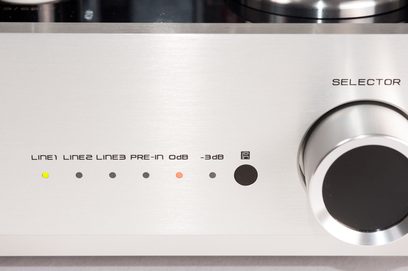 Vista parcial frontal do amplificador integrado estéreo valvulado Cayin CS-300A prata, painel em alumínio escovado prateado com grande botão circular preto e prata à direita e fileira central de LEDs coloridos acompanhados de inscrições serigrafadas
