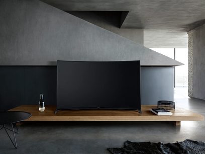 Black Panasonic TX-65CR850 TV placed on a wooden cabinet in a room with gray walls and concrete floor, front view